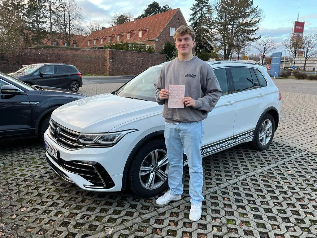 Fahrschüler mit Prüfungsbescheinigung vor dem Fahrschulwagen